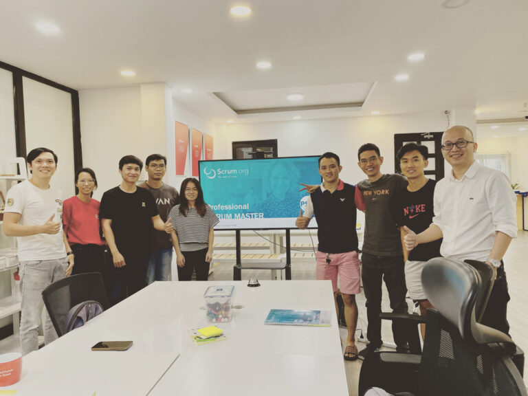 Học viên chụp ảnh cùng trainer trong phòng học, màn hình chiếu Professional Scrum Master