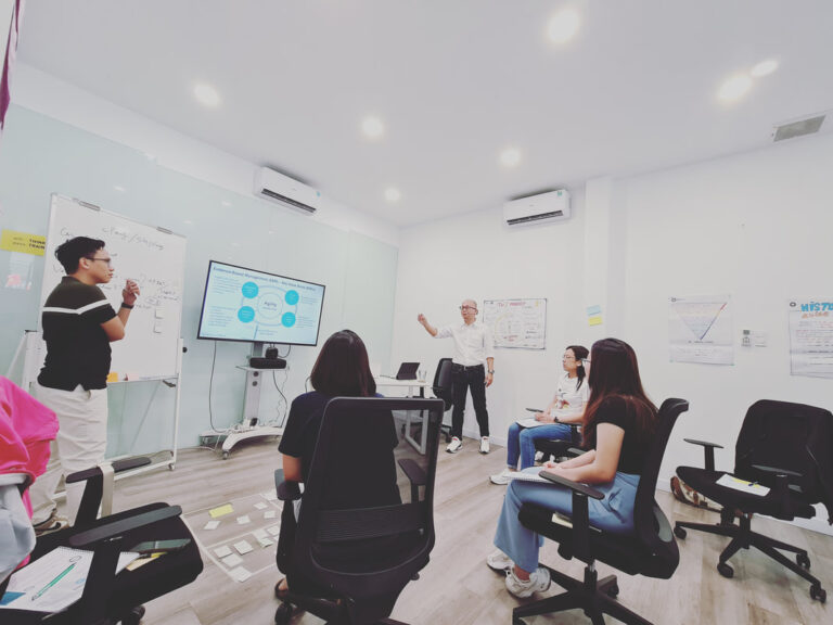 Trainer giảng bài trước lớp, học viên ngồi theo dõi