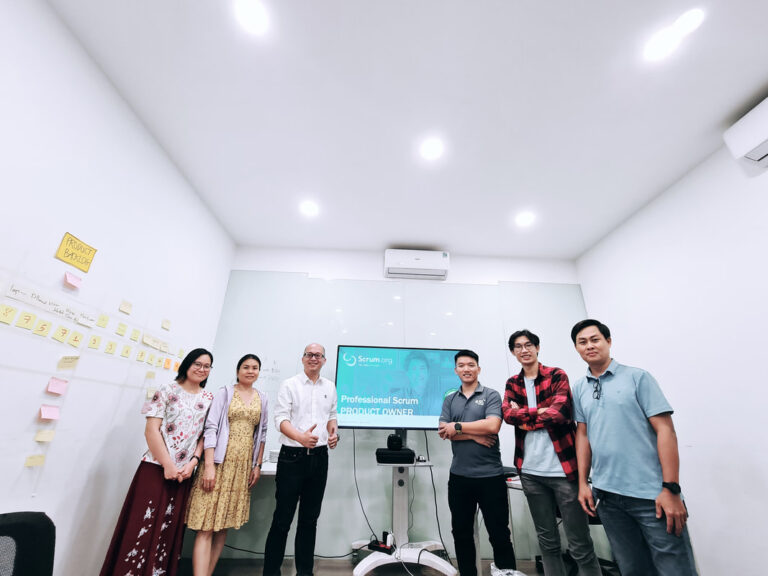 Trainer và học viên đứng trước màn hình khoá học, tường dán ghi chú