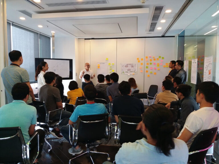 Trainer trình bày trước lớp, tường dán đầy ghi chú